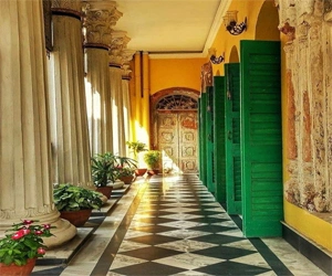 Sardar Bari corridor with columns, green wooden doors, and a patterned floor in Sonargaon.