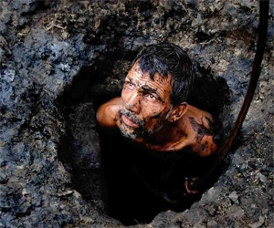 A man emerging from a muddy pit in Dhaka, covered in mud, looking upward, symbolising intense human labour and survival.
