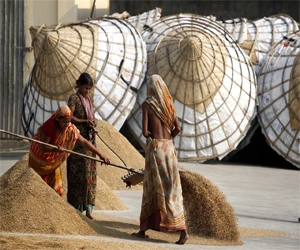 Traditional rice processing scene with local women working beside large woven storage structures.