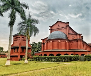 Oxford Mission Church heritage building surrounded by palm trees and green lawns in Barisal, Bangladesh.