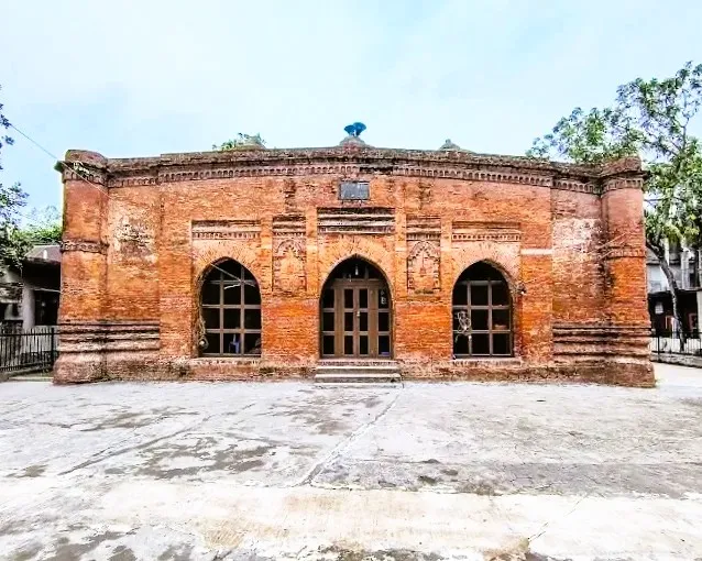 The weathered red brick facade of Baba Adam’s Mosque featuring three pointed arched entrances and intricate terracotta ornamentation characteristic of the Sultanate period.