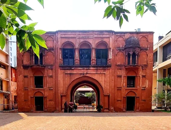 A historic two-story red brick gateway with a large central archway and smaller windows, representing 18th-century Mughal-style architecture in Dhaka.