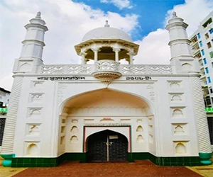The white facade of Shah Suja Mosque in Cumilla features a central dome with an ornate pavilion, four corner minarets, and a large arched entrance under a bright sky.