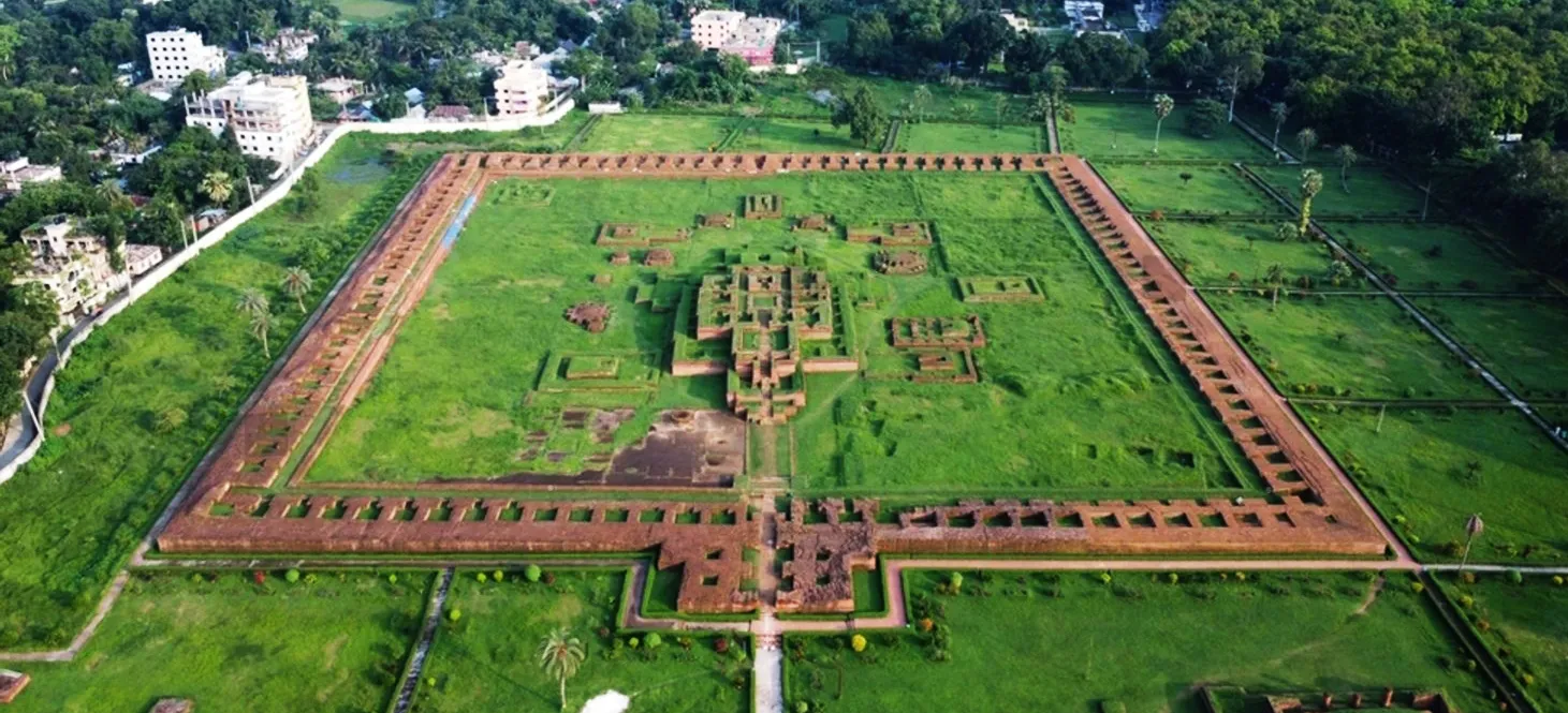 An aerial view of the massive square archaeological site of Shalban Vihara in Mainamati, Comilla, showing the red brick foundations and a central temple surrounded by lush green lawns.