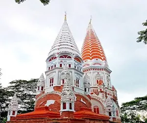 Two towering, intricately decorated white and orange spires of the Sonarong Jora Moth temples reaching toward the sky, surrounded by greenery.