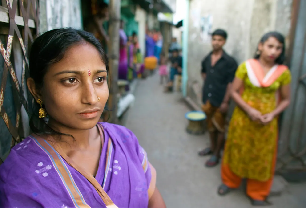 A Bangladeshi woman wearing a purple sari looking thoughtfully away from the camera in a narrow alleyway of a historic brothel village in Bangladesh.